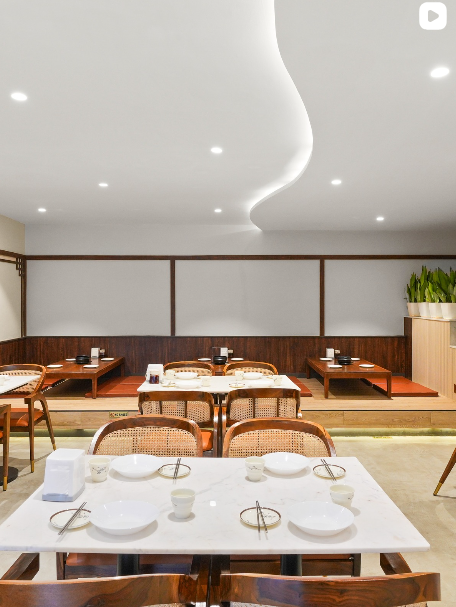 Restaurant interior with curved false ceiling, timber panelling and marble tables